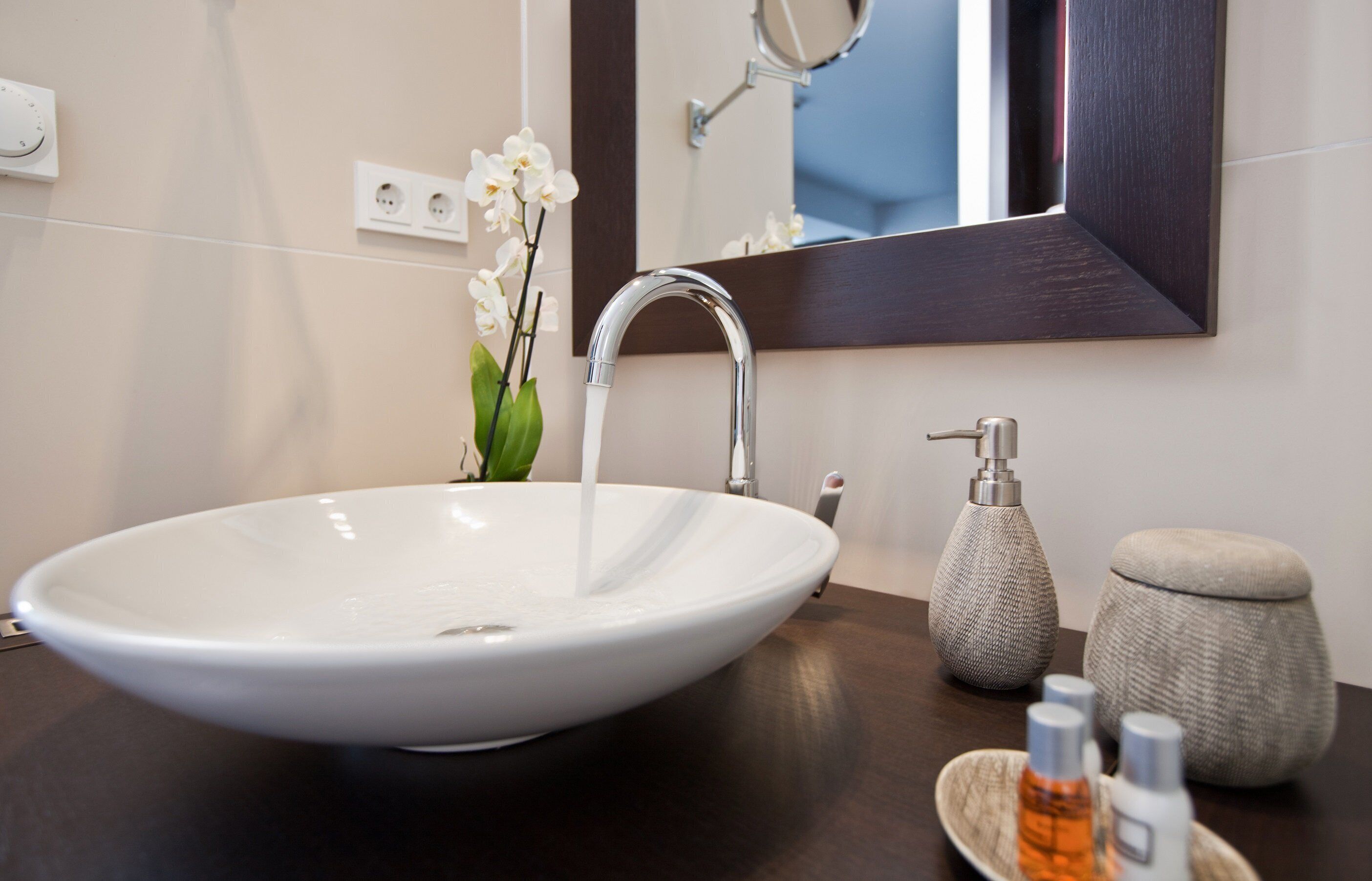 Un baño con un lavabo blanco, un espejo y un florero con flores.