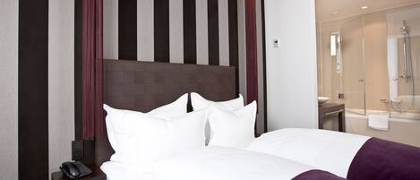 A hotel room with a large bed, a bedside phone, a mirror, and a bathroom with a shower and sink.