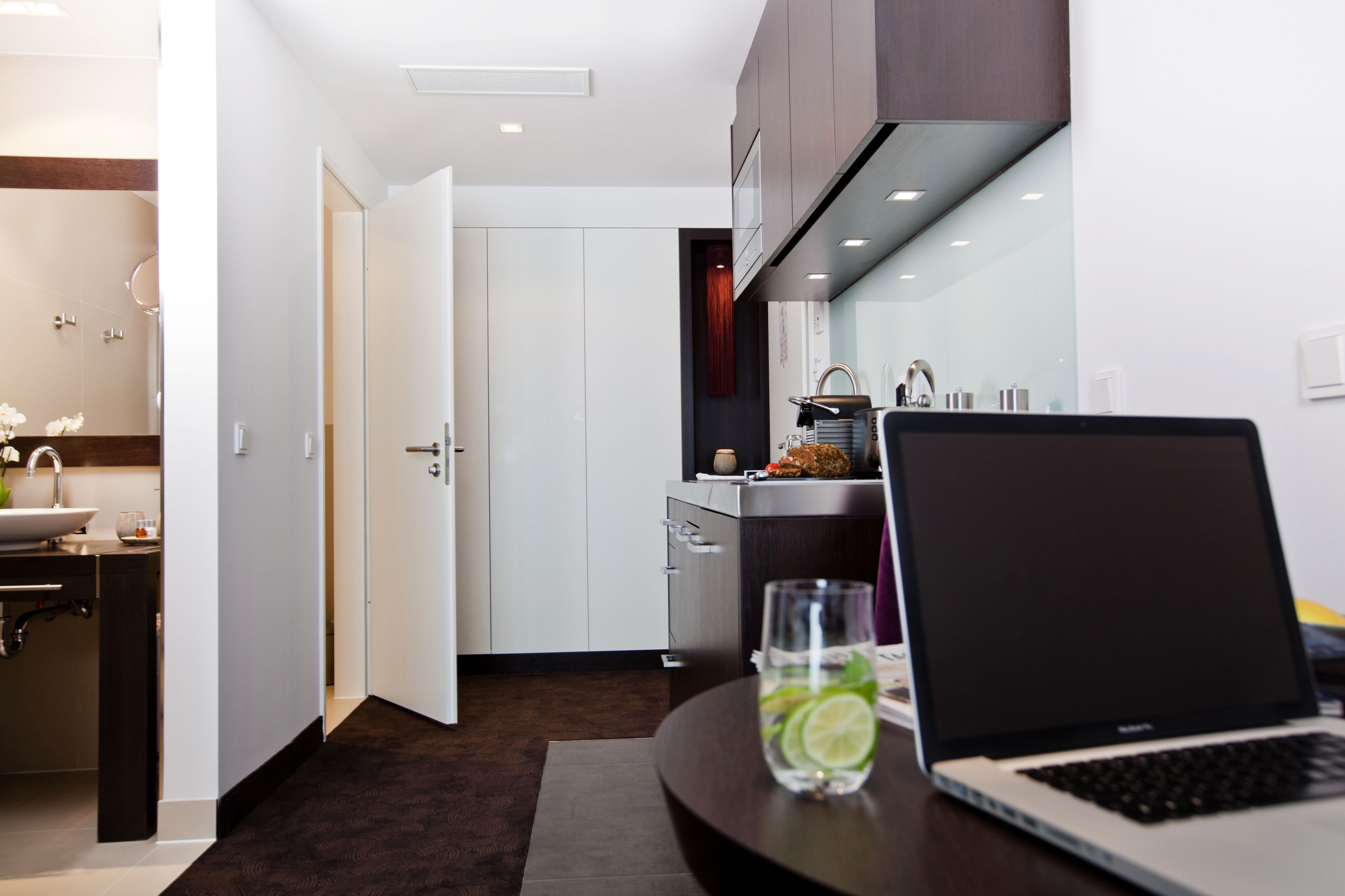 A modern kitchen with a laptop on a table, a glass of water, and a door leading to another room.
