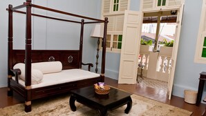A four-poster bed with a wooden frame and white bedding, a small table with a basket, and a view of a balcony with white railings. - PalanquInn Heritage Suites (George Town)