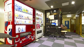 A vending machine with various drink options and a chair in a room with a checkered floor. - Business Hotel Wako (Osaka)