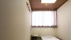 A small, single-bed room with a window, a bedside table, and a wall-mounted light fixture. - Business Hotel Wako (Osaka)