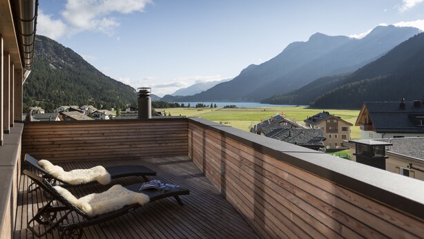 Una terraza de madera con sillones de descanso y vistas a un lago y montañas.