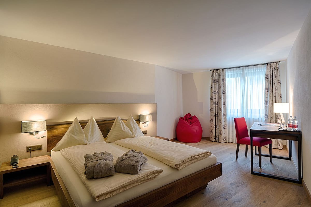 A hotel room with a bed, bedside tables, a desk, a chair, and a red bean bag.