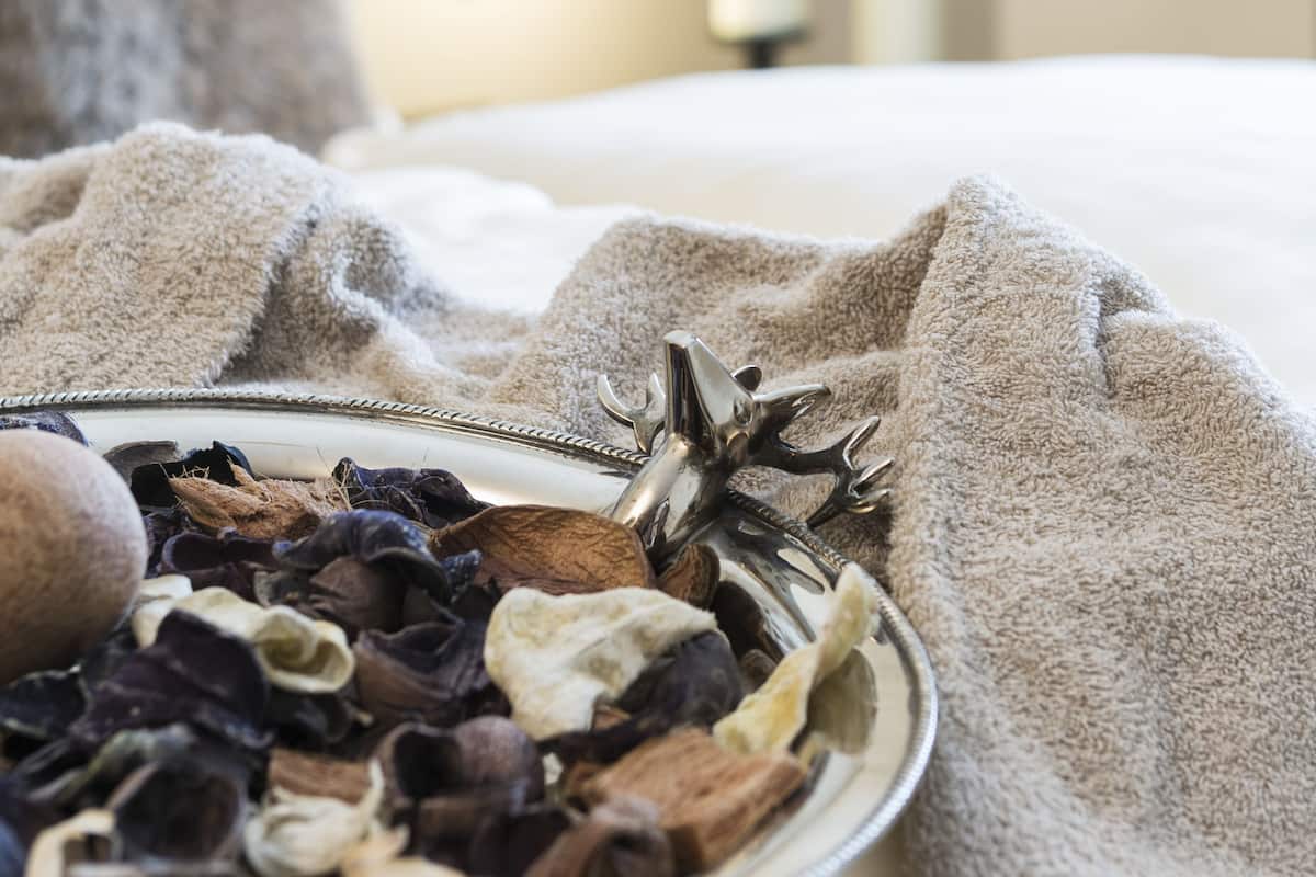 A bed with a decorative plate of dried flowers and a candle holder, a bedside lamp, and a lit candle in a hotel room.
