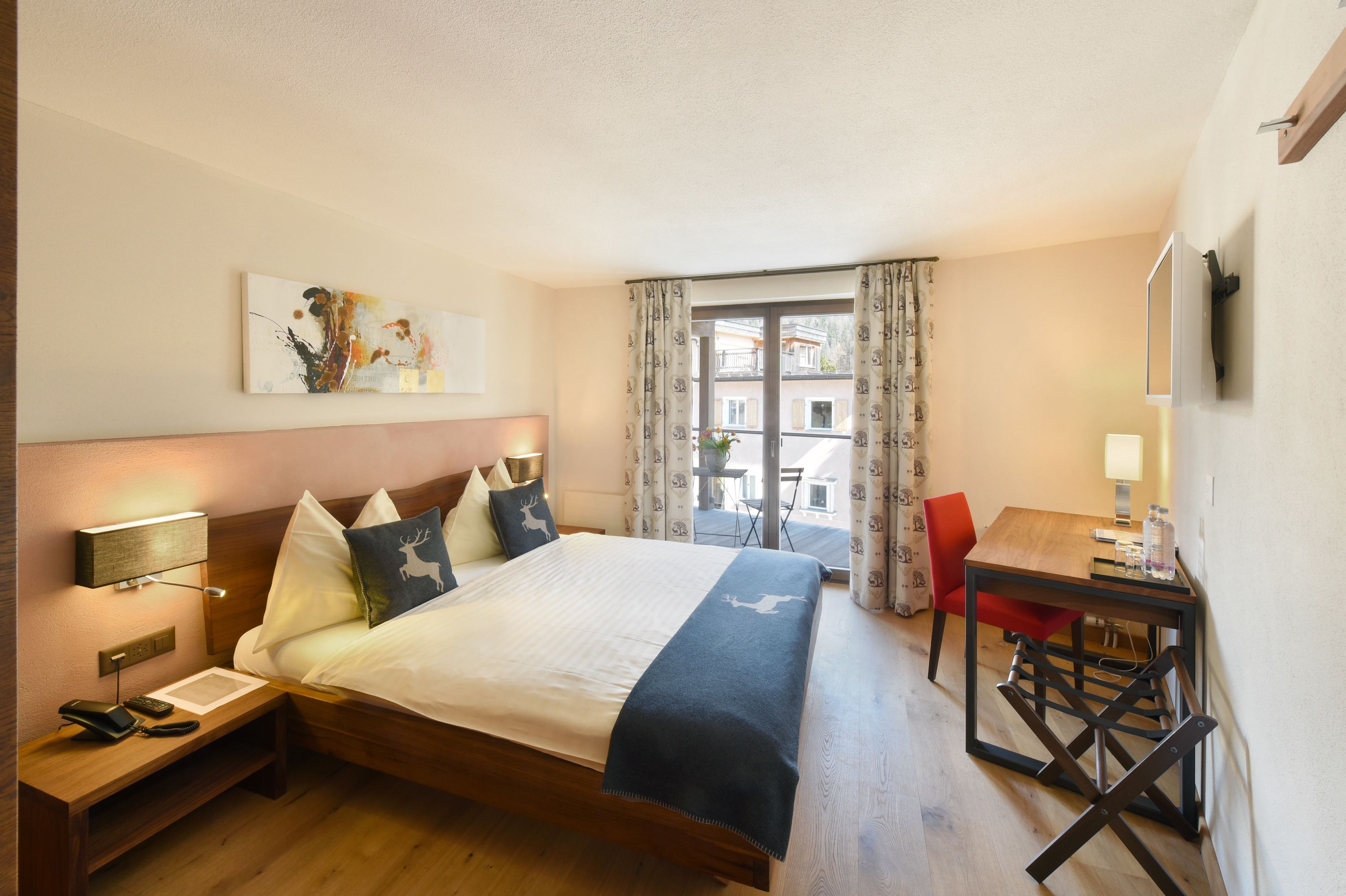 Habitación de hotel con cama, mesita de noche, lámpara y vistas al exterior.