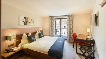 Habitación de hotel con cama, mesita de noche, lámpara y vistas al exterior.