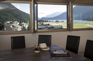 Un comedor con una mesa, sillas, una laptop, un sombrero y un cuenco de flores.