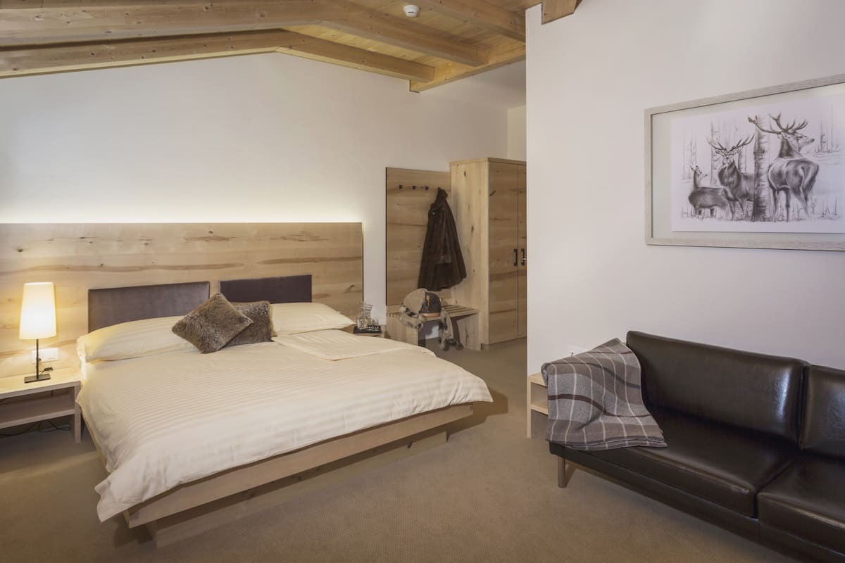 A bedroom with a wooden bed, a nightstand with a lamp, a wooden wardrobe, a framed wildlife painting, and a leather sofa.