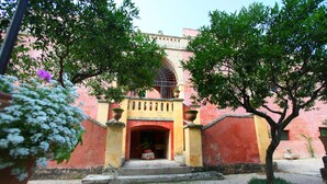 A courtyard with a red building, a central archway, and potted plants. - Palazzo Laura (Morciano di Leuca)