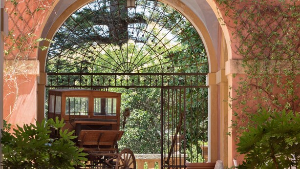 An arched entrance with a wrought iron gate, a wooden carriage, and potted plants. - Palazzo Laura (Morciano di Leuca)