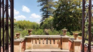 Ein schmiedeisernes Tor mit Steinbalustrade führt zu einem Garten mit Kübelpflanzen und Bäumen.
