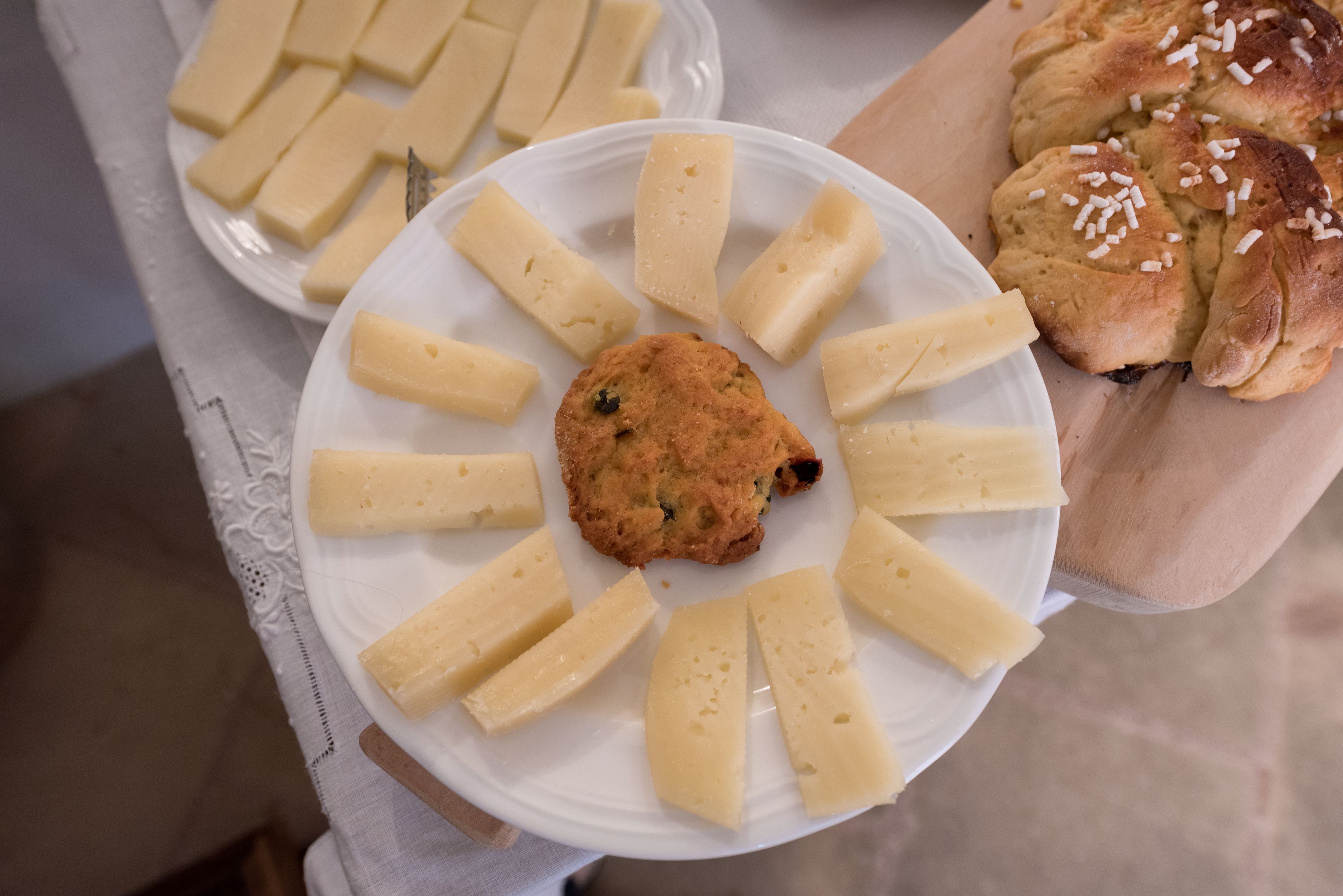 A plate with a cookie and cheese slices, and a wooden board with bread.