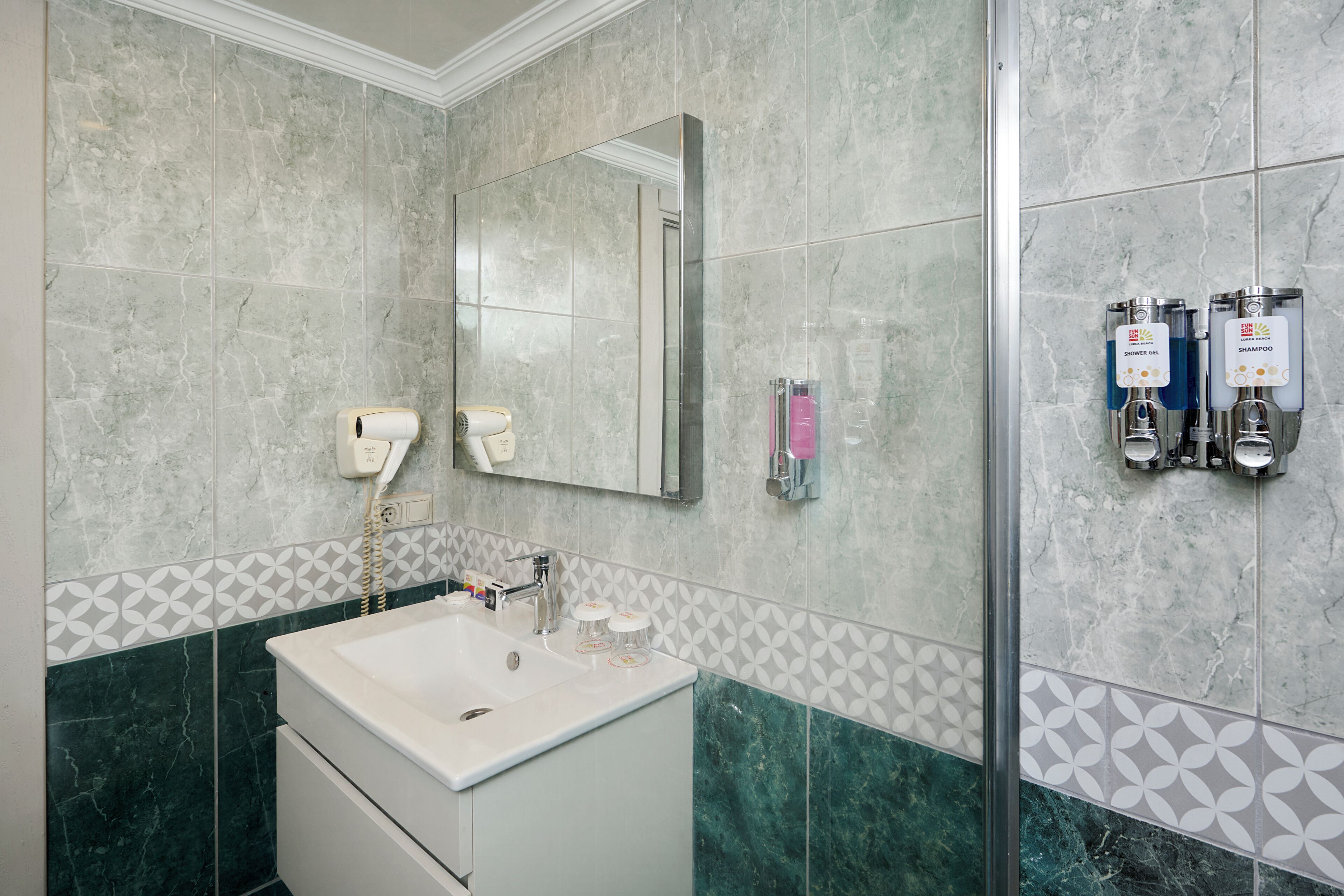 A bathroom with a sink, mirror, towel dispenser, and shower gel and shampoo dispensers.
