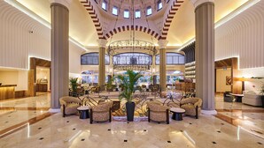 A spacious lobby with a central chandelier, seating arrangements, and a large plant.