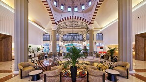 A spacious lobby with a central seating area, a large chandelier, and a view of the interior through arched windows.