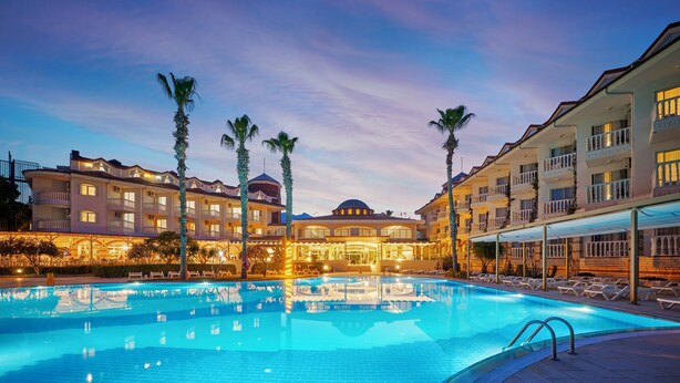 A hotel with a swimming pool, multiple balconies, and palm trees.