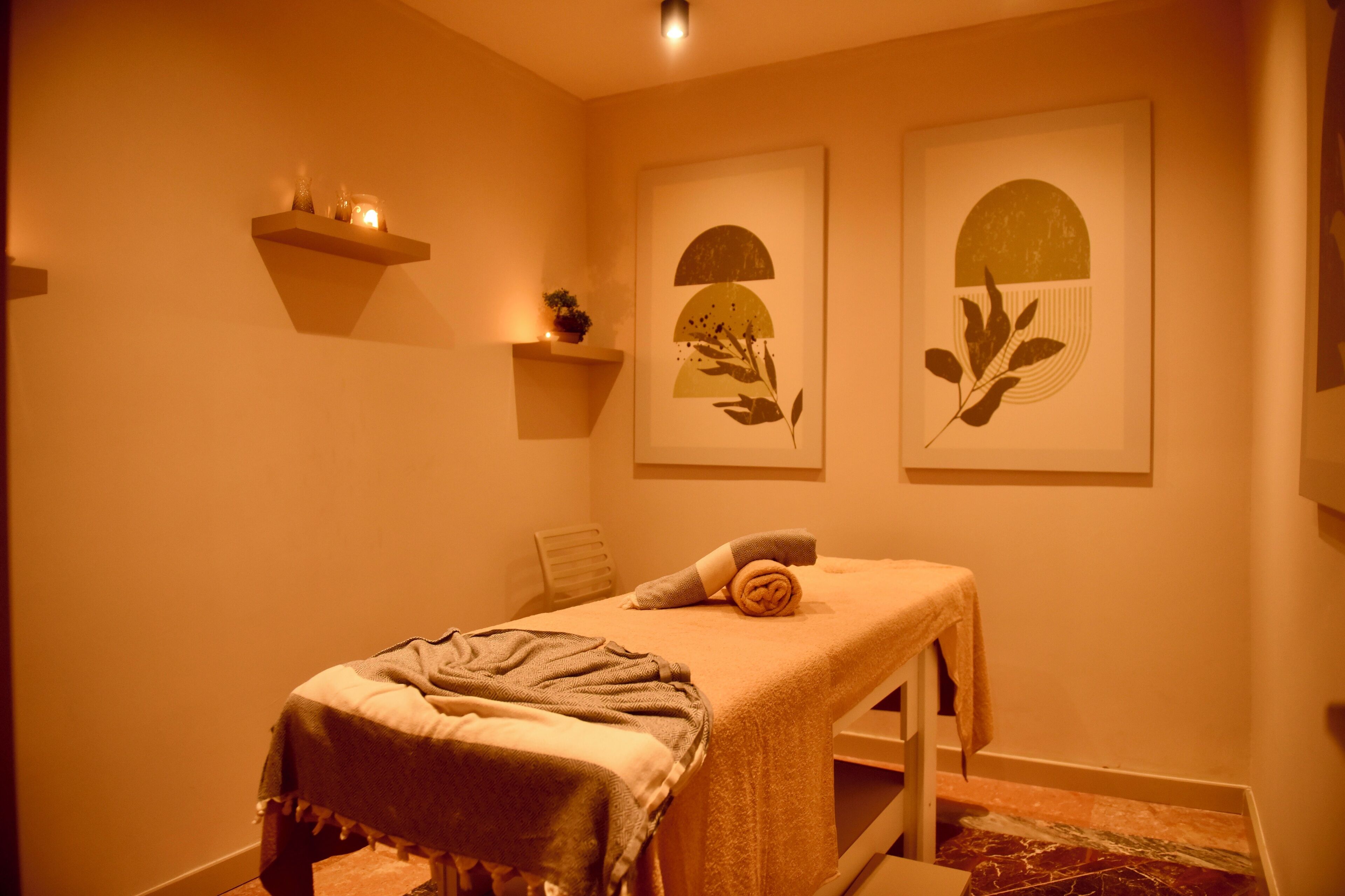 A massage therapy room with a massage table, towels, and wall-mounted shelves with candles and a small plant.