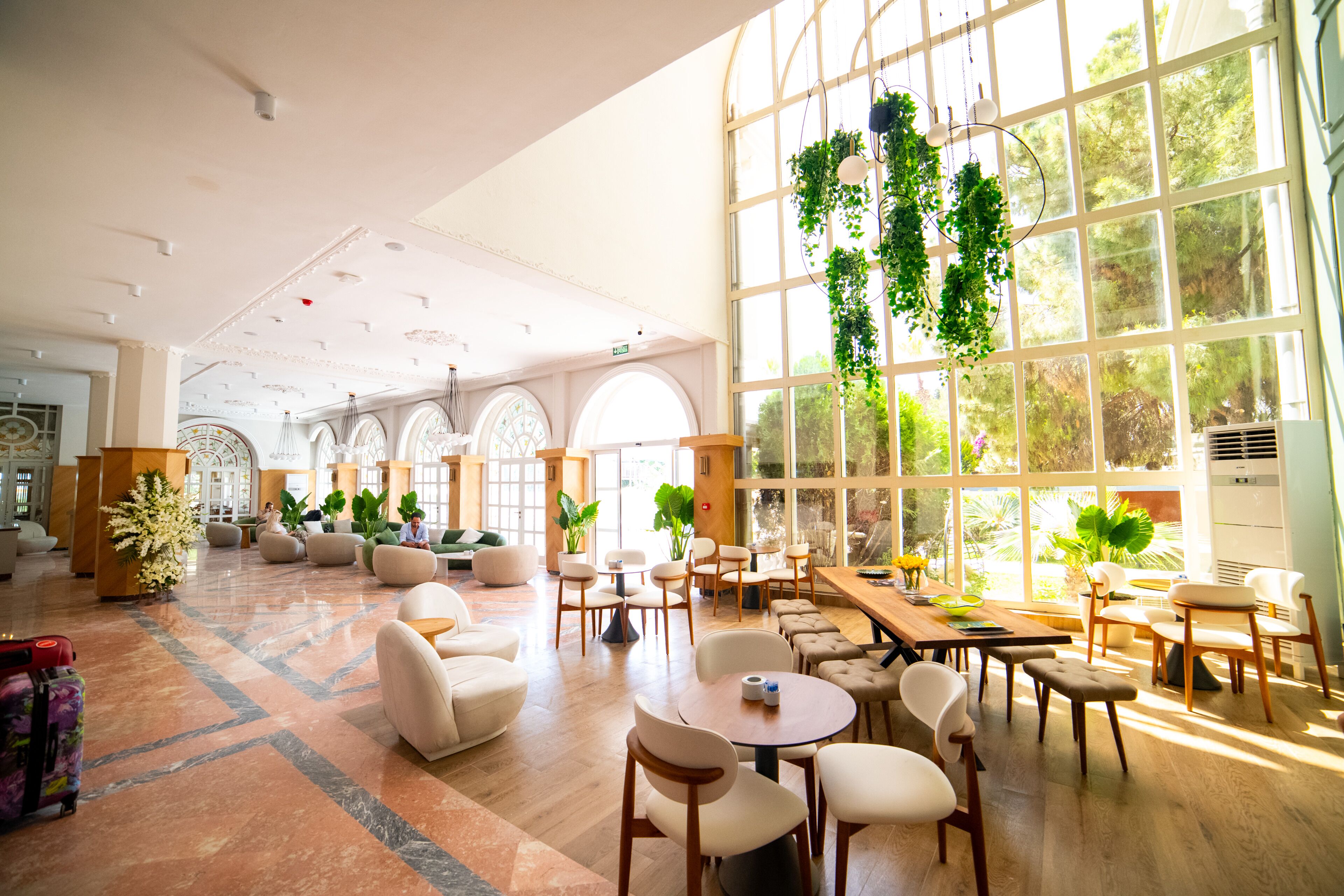 Een ruime lobby met een grote zithoek, een receptiebalie en grote ramen met beplanting.