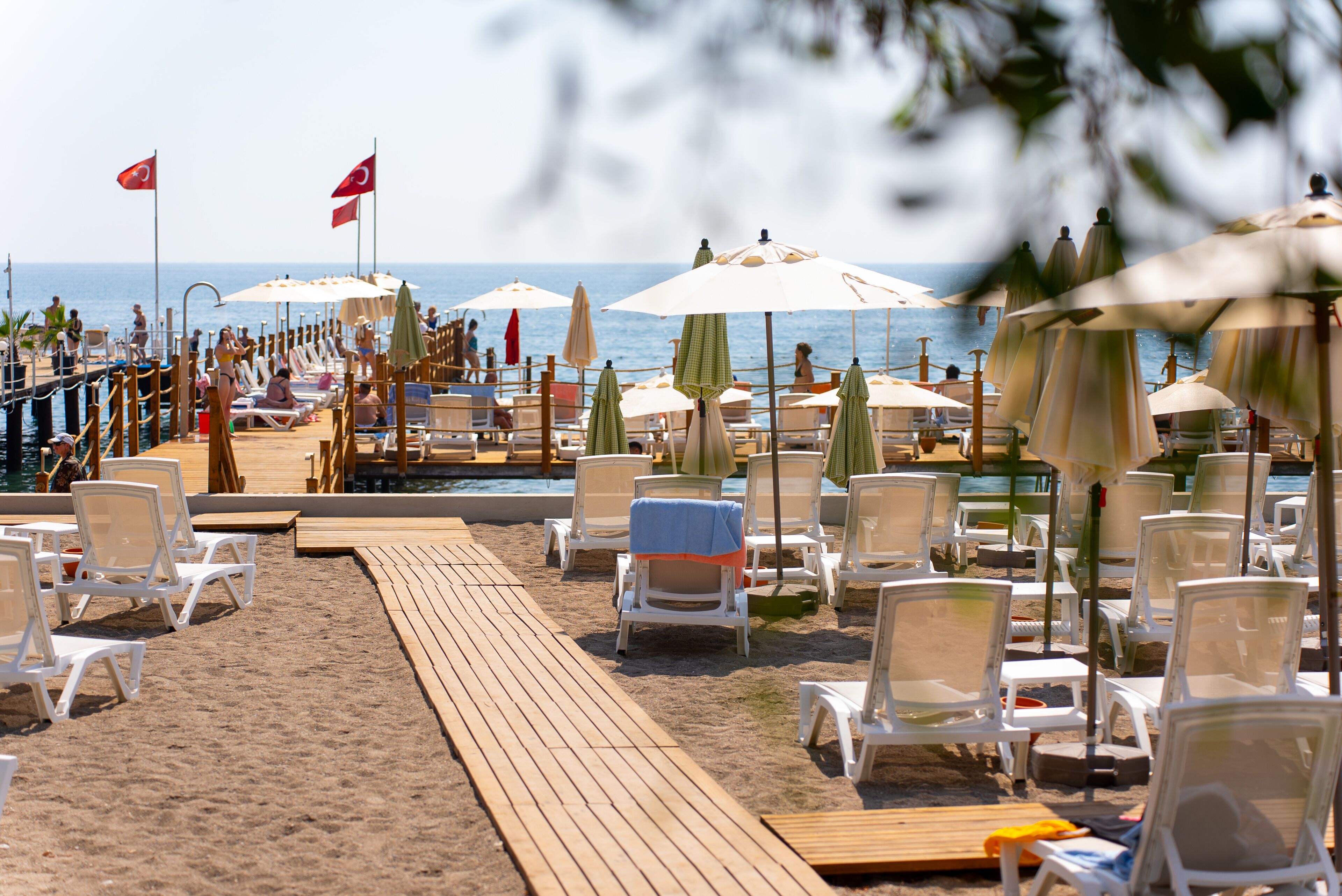 A beachside resort with rows of sun loungers and umbrellas, a wooden deck, and a view of the sea.