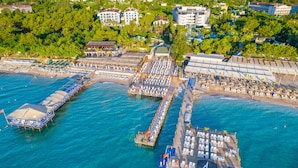 Vista aérea de un complejo turístico costero con un muelle que se adentra en el mar, con tumbonas y una zona de estar cubierta.