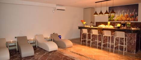 A modern lounge area with reclining chairs, a bar with stools, and a marble floor.