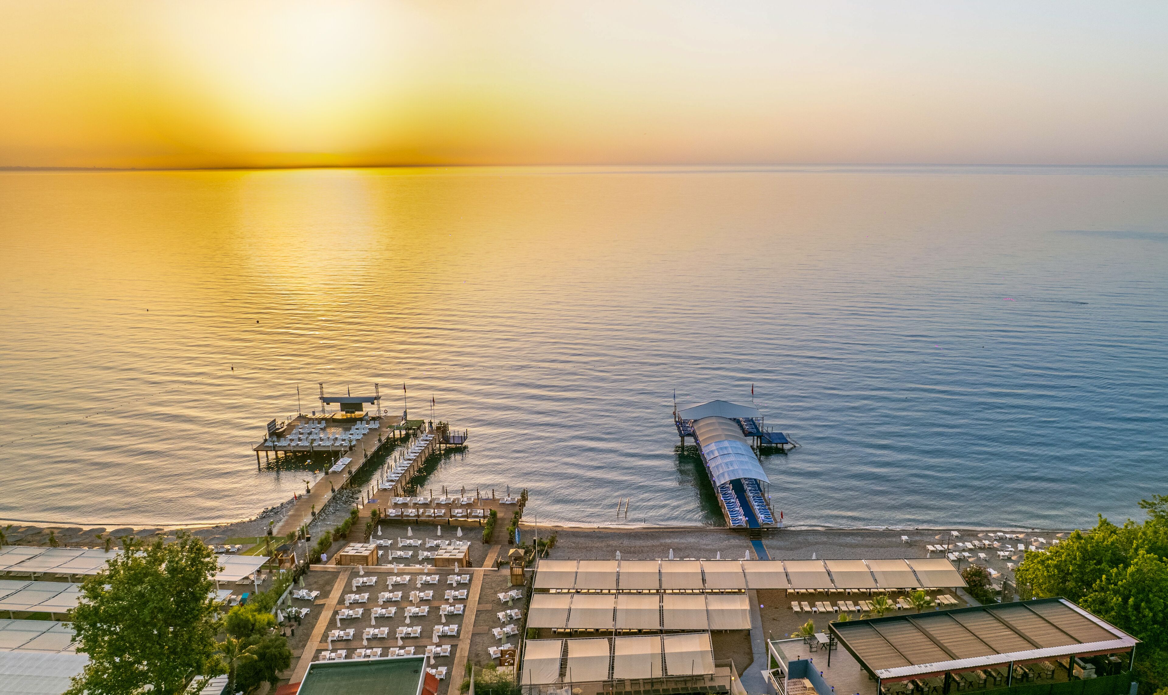 Un resort costero con un muelle que se adentra en el mar, ofreciendo tumbonas y una zona de estar cubierta.