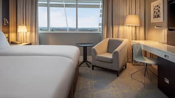 A hotel room with a large bed, a desk, a chair, a small table, and a window with curtains.