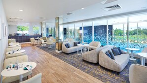 A modern hotel lobby with a mix of seating areas, a reception desk, and large windows offering a view of greenery.