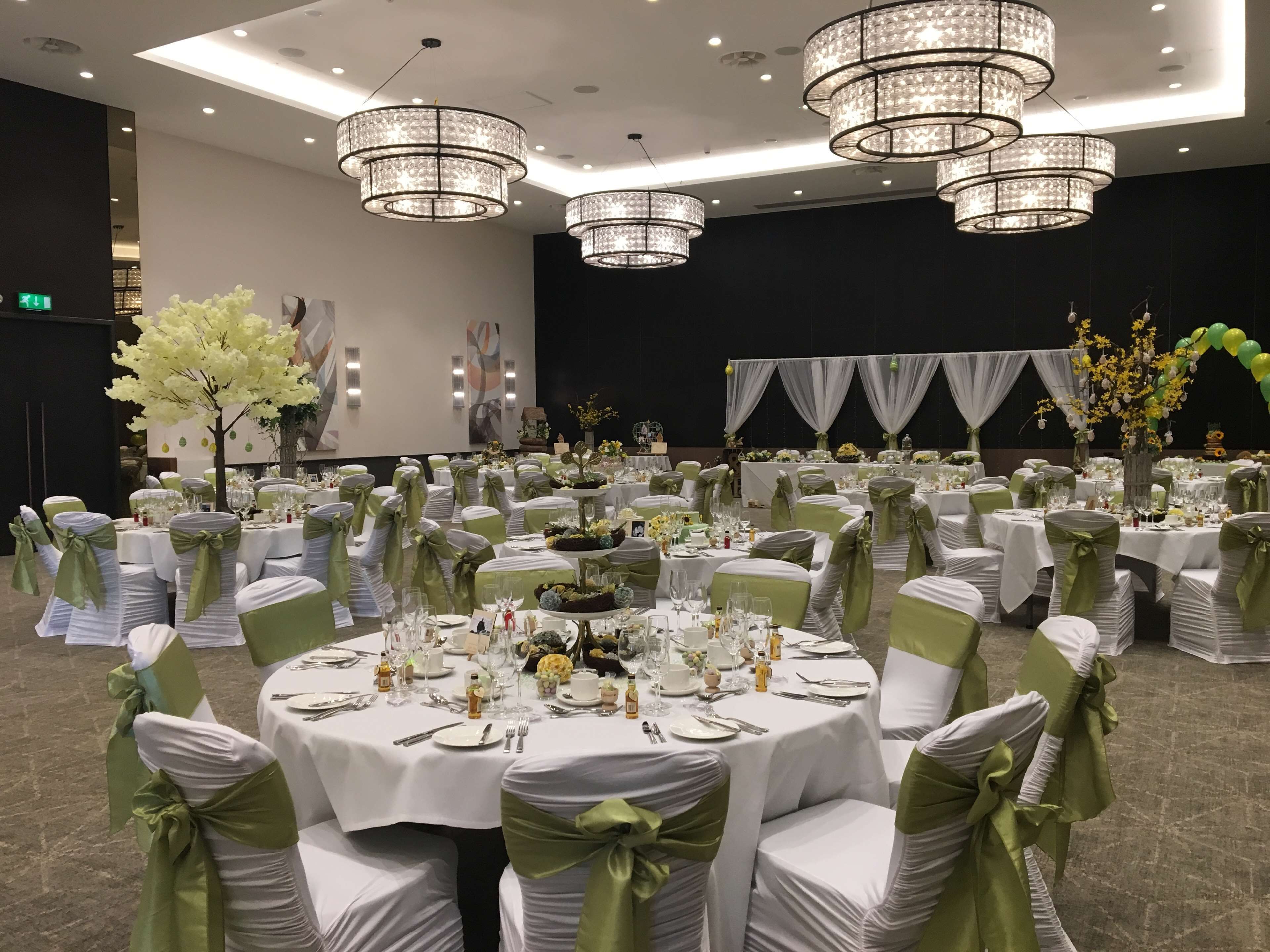 A banquet hall with round tables, green sashes, and chandeliers.