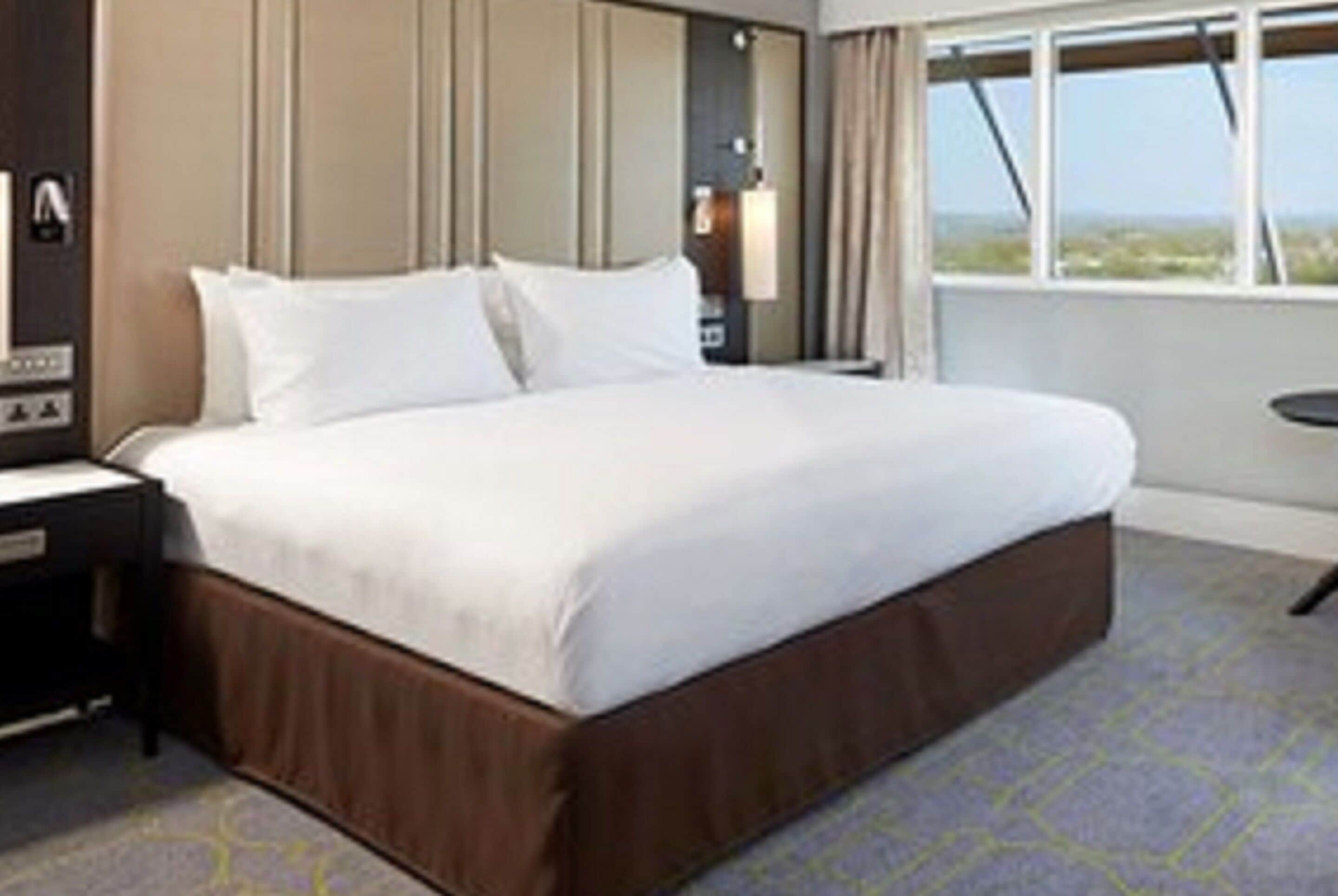 A hotel room with a large bed, a nightstand, and a window with a view.