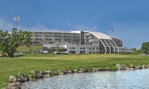 Enjoy panoramic views of the surrounding area from this hotel's unique roof structure, situated on a grassy hill near a body of water and a golf course.