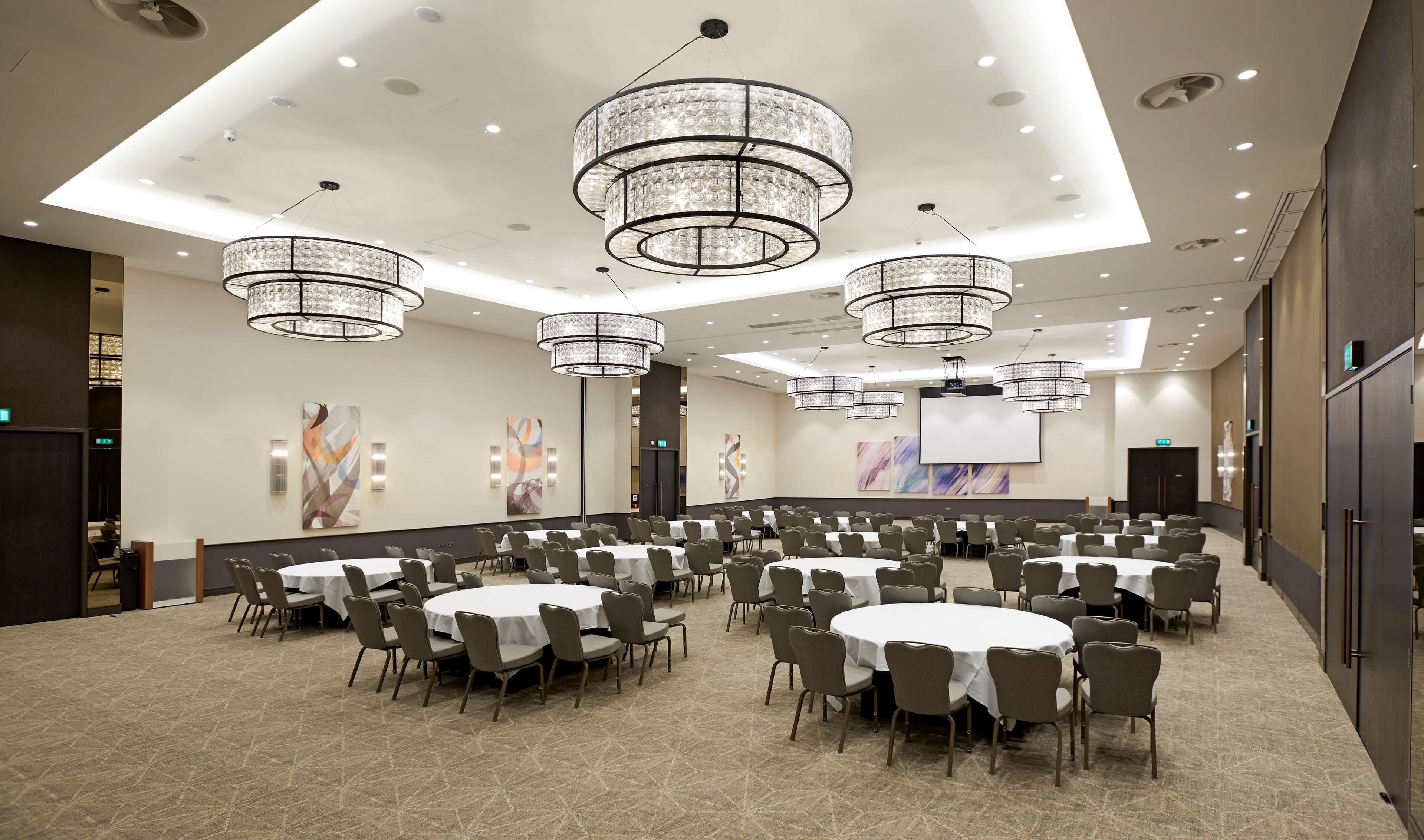 A conference room with multiple round tables, grey chairs, and large chandeliers.