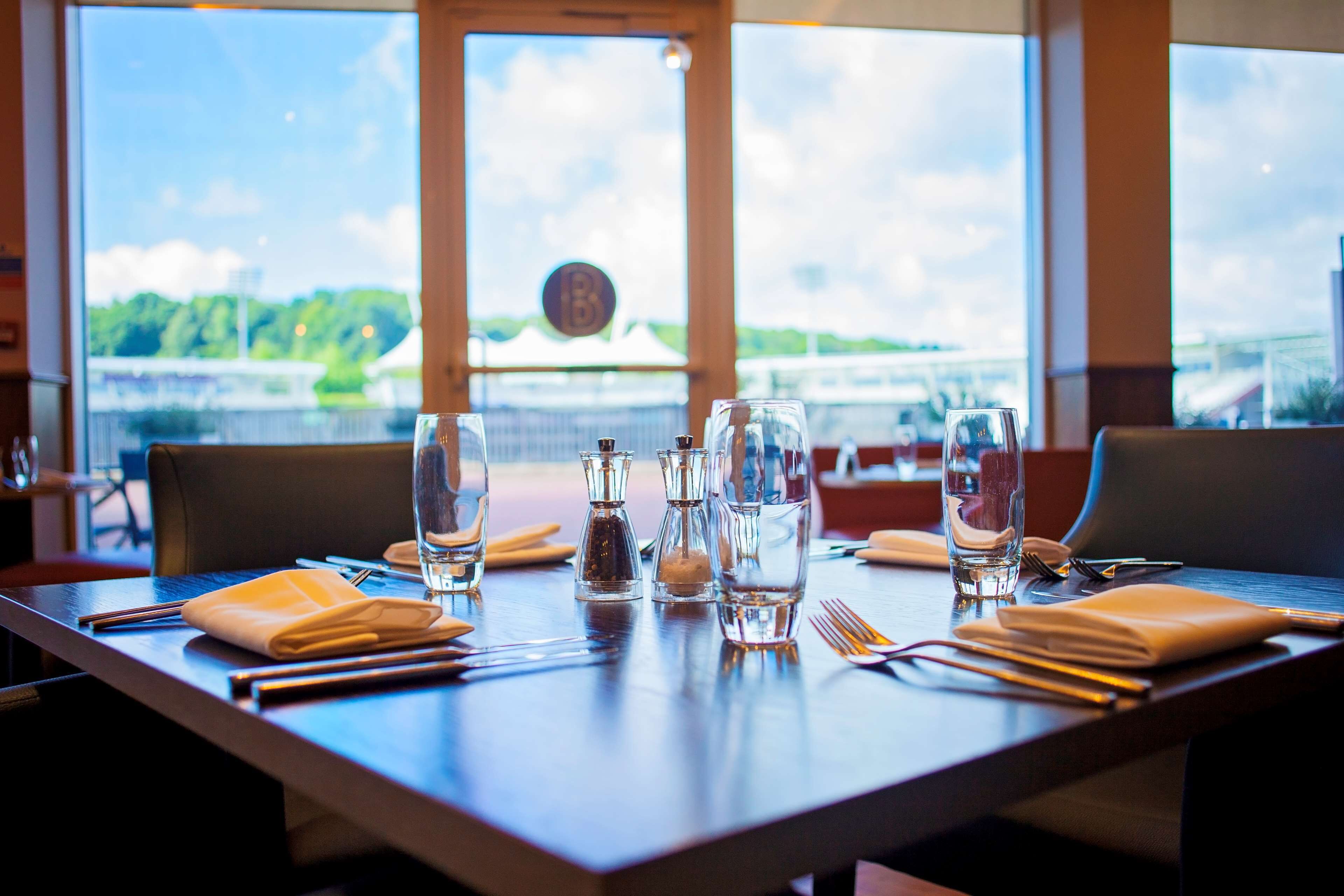A dining table set with glasses, cutlery, and napkins, with a view of a body of water and a bridge in the background.