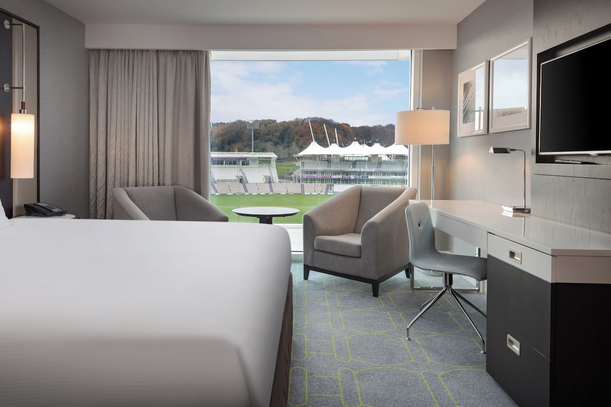 Een hotelkamer met een bed, twee fauteuils, een bureau, een televisie en uitzicht op een stadion.