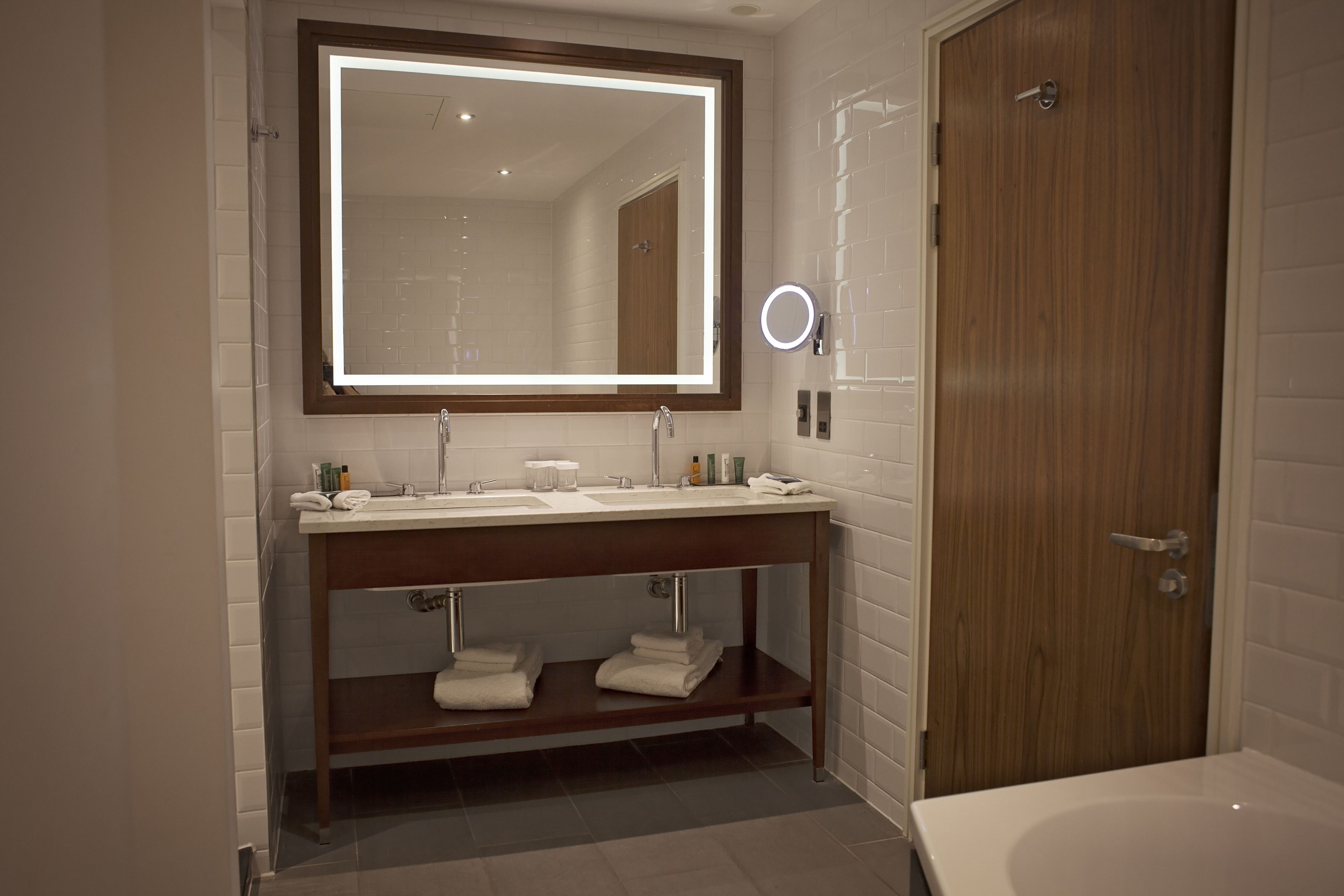 A modern bathroom with a large mirror, dual sinks, a vanity, and a bathtub.