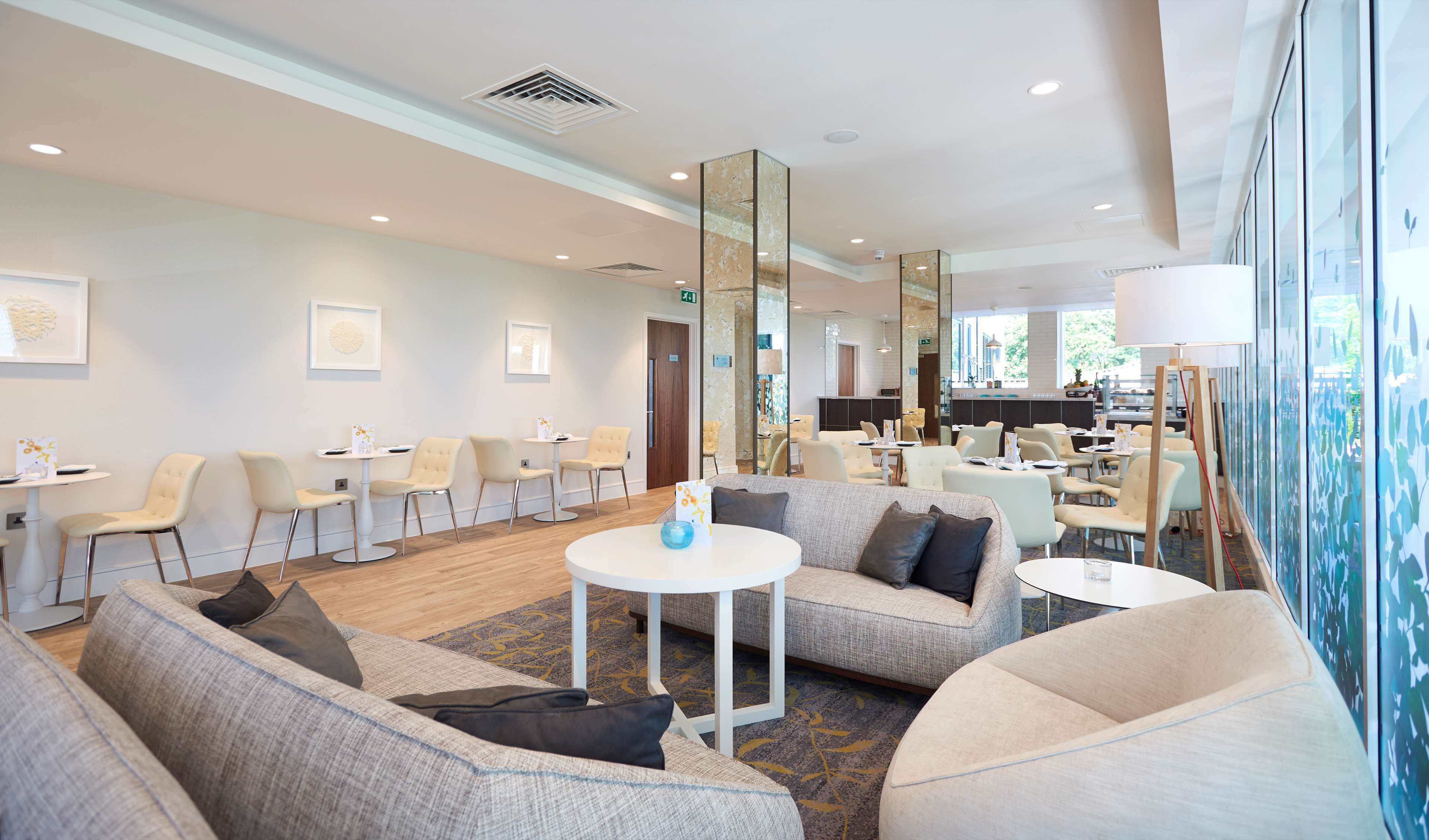 A modern hotel lobby with seating areas, a reception desk, and a large window offering a view of the outdoors.