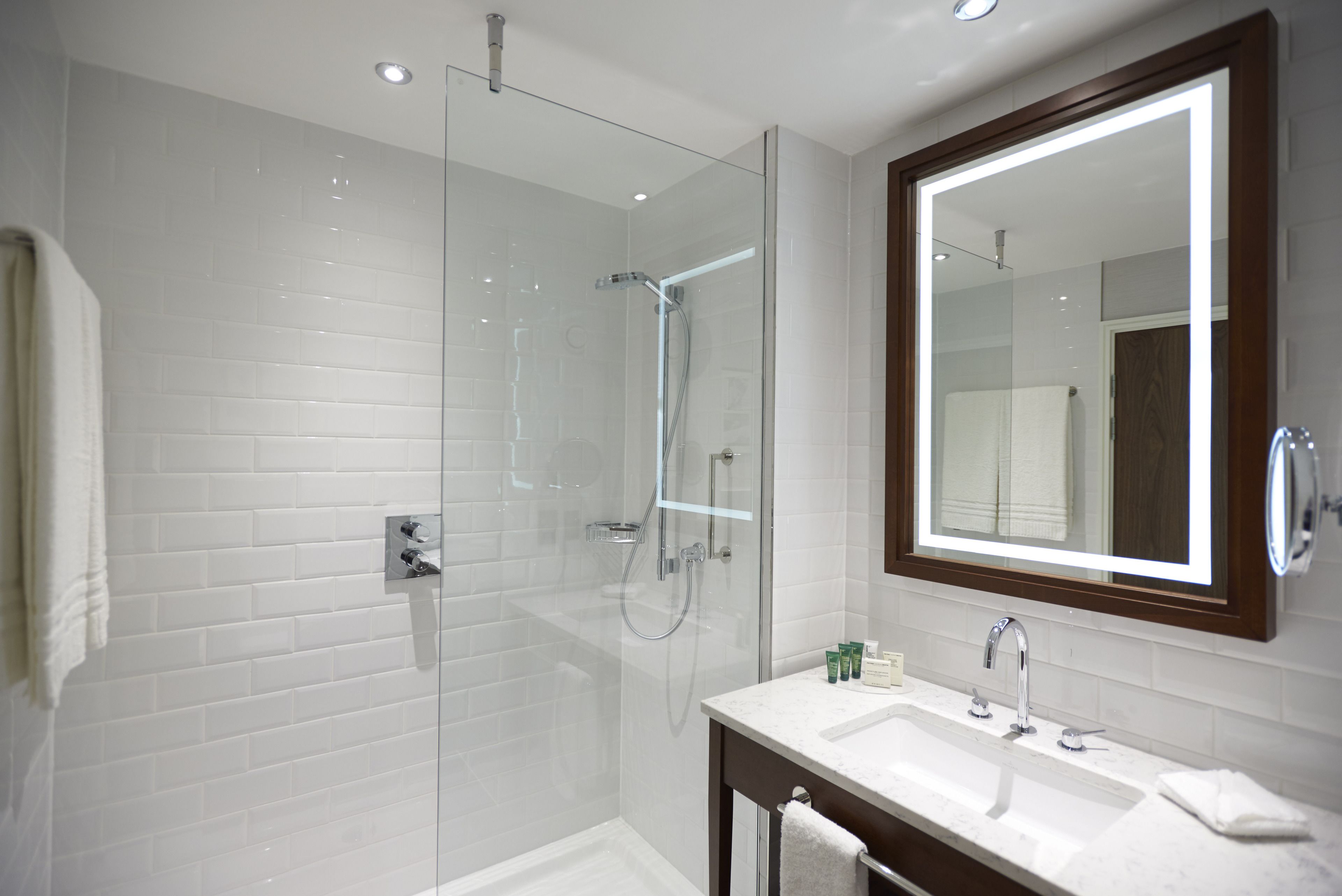 A modern bathroom with a glass-enclosed shower, a large mirror, and a white-tiled wall.