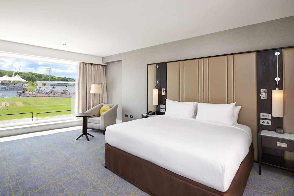 Een hotelkamer met een groot bed, een bureau, een stoel en uitzicht op een sportveld.