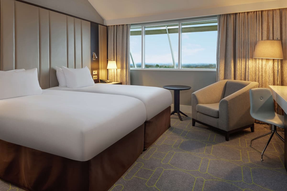 Een hotelkamer met twee bedden, een bureau, een stoel, een lamp en een raam met gordijnen.