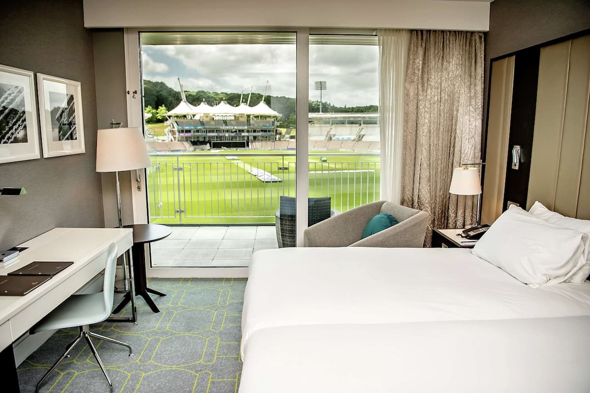 Een hotelkamer met een bed, bureau, stoel en uitzicht op een sportveld.