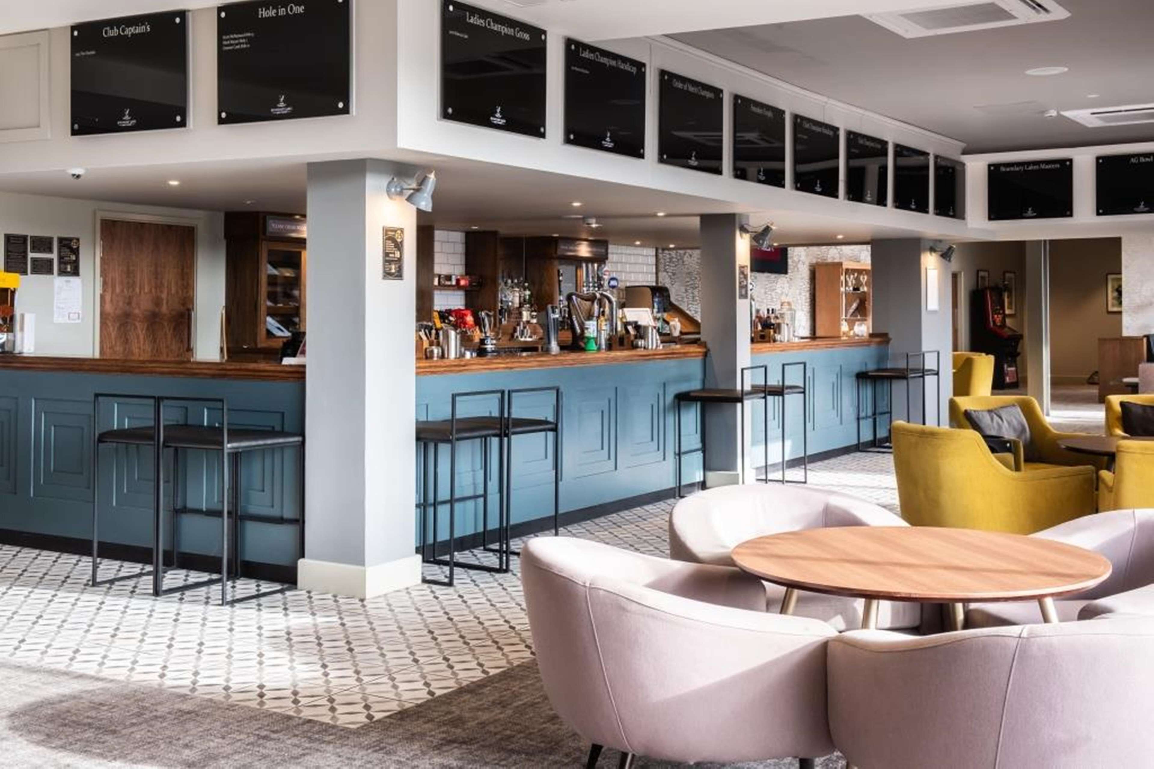 A modern bar area with a counter, stools, and seating. There are framed certificates on the wall.