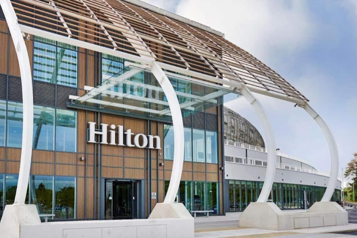 A modern hotel building with a prominent 'Hilton' sign, large glass windows, and a unique curved architectural feature.