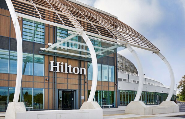 Experience the sleek, curved facade of Hilton Hotel, featuring a distinctive wooden roof and prominent building signage.