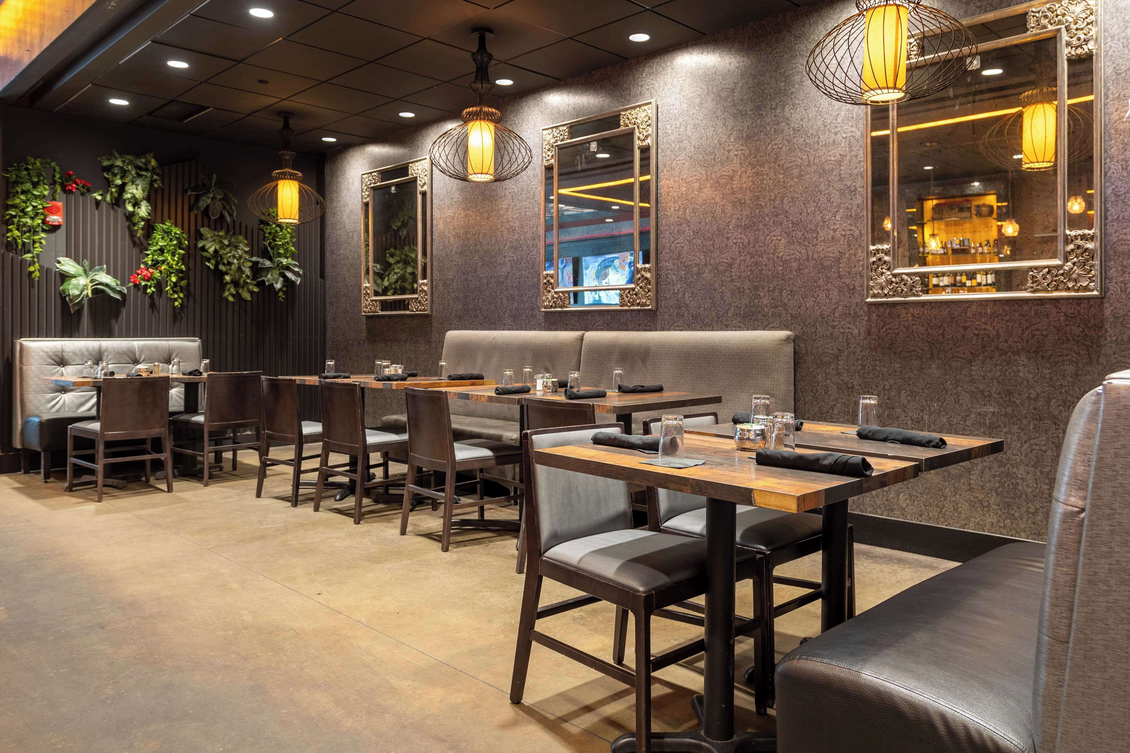 Un restaurant avec des banquettes et des tables, un plancher en bois et des plantes décoratives sur les murs.