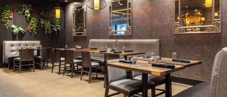 Un restaurant avec des banquettes et des tables, un plancher en bois et des plantes décoratives sur les murs.