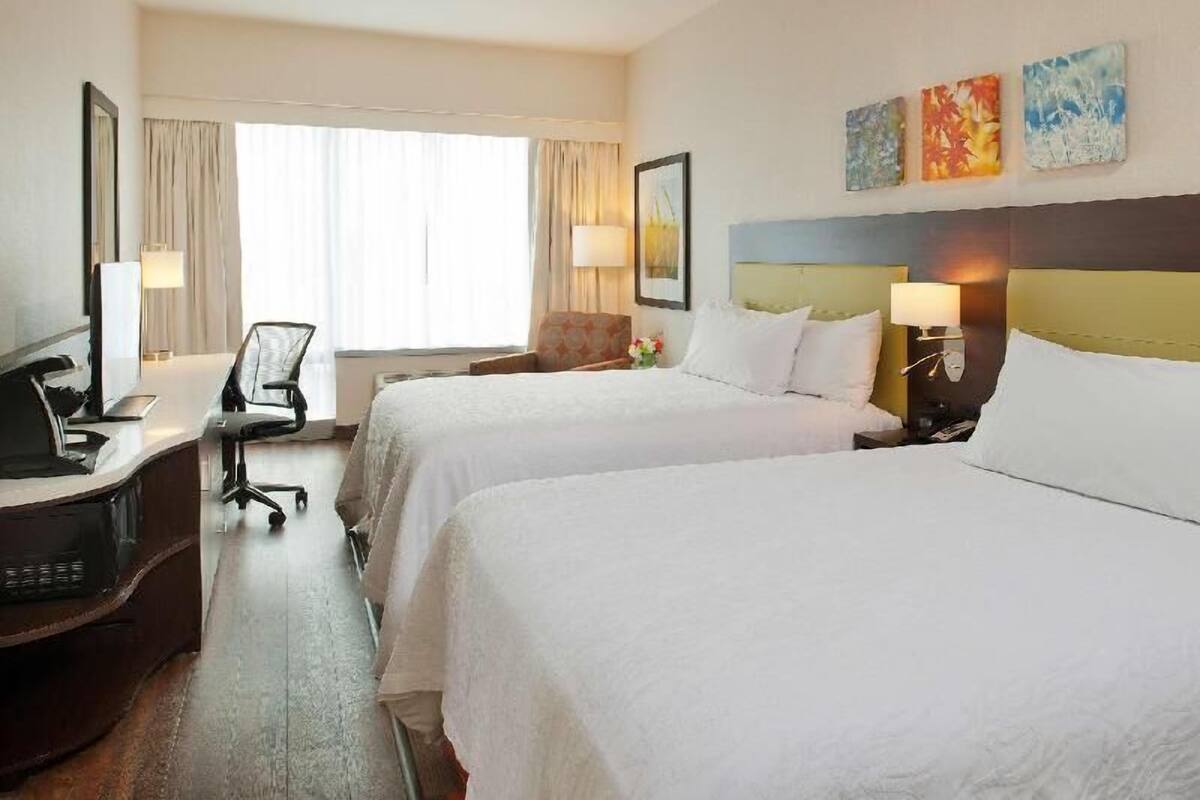 A hotel room with two beds, a desk with a computer, a chair, and a window with curtains.