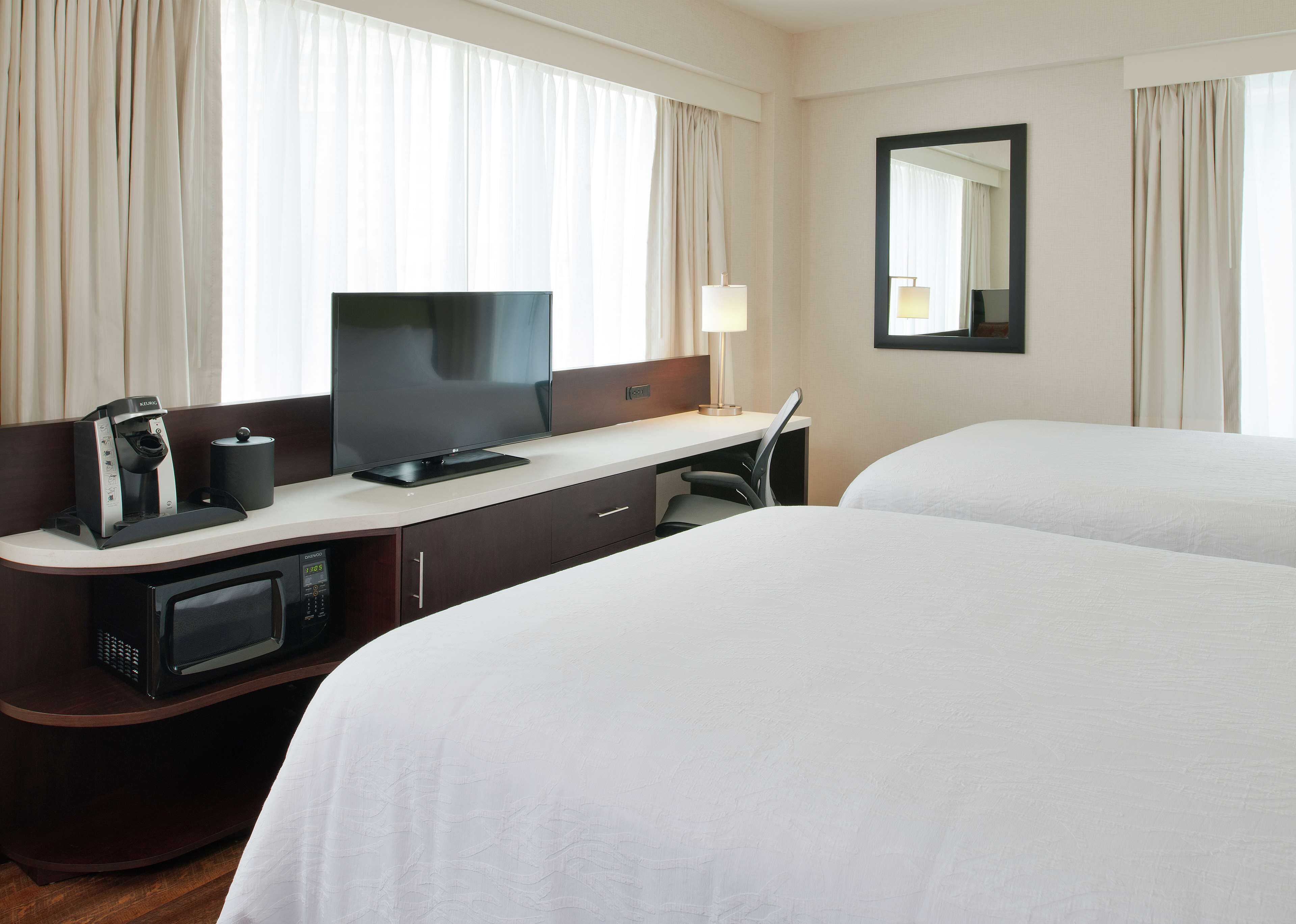 Quarto de hotel com cama, escrivaninha com televisão, máquina de café e micro-ondas.