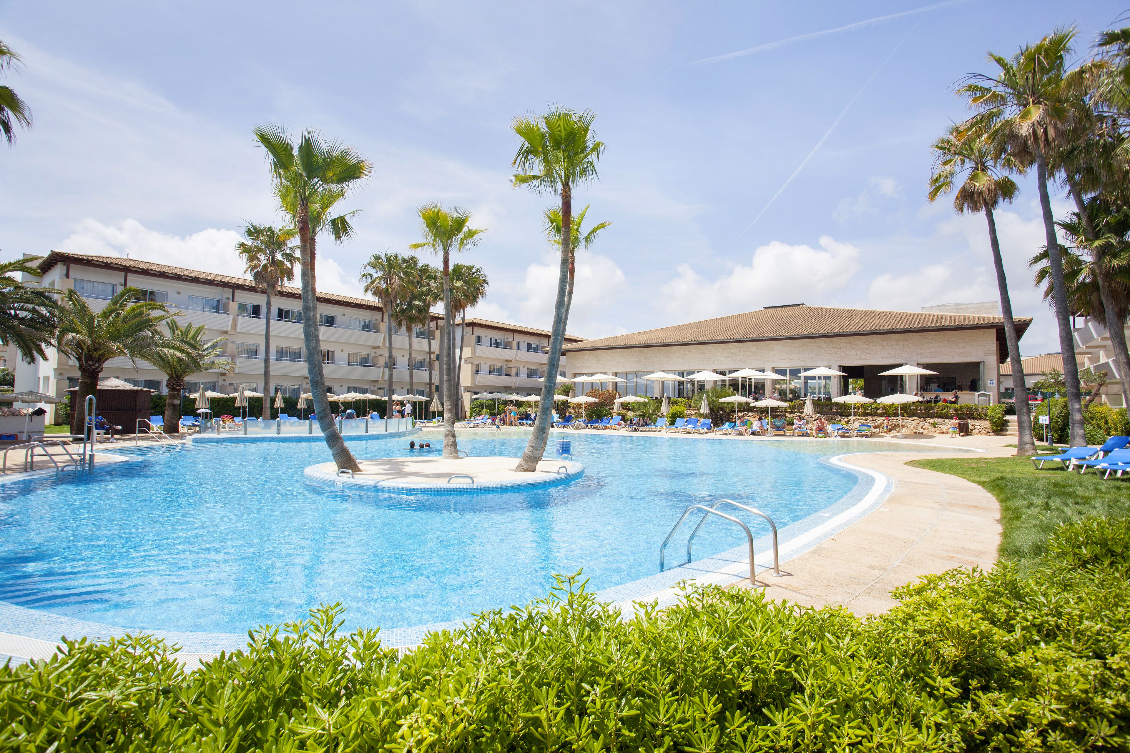 A swimming pool with palm trees, lounge chairs, and umbrellas.