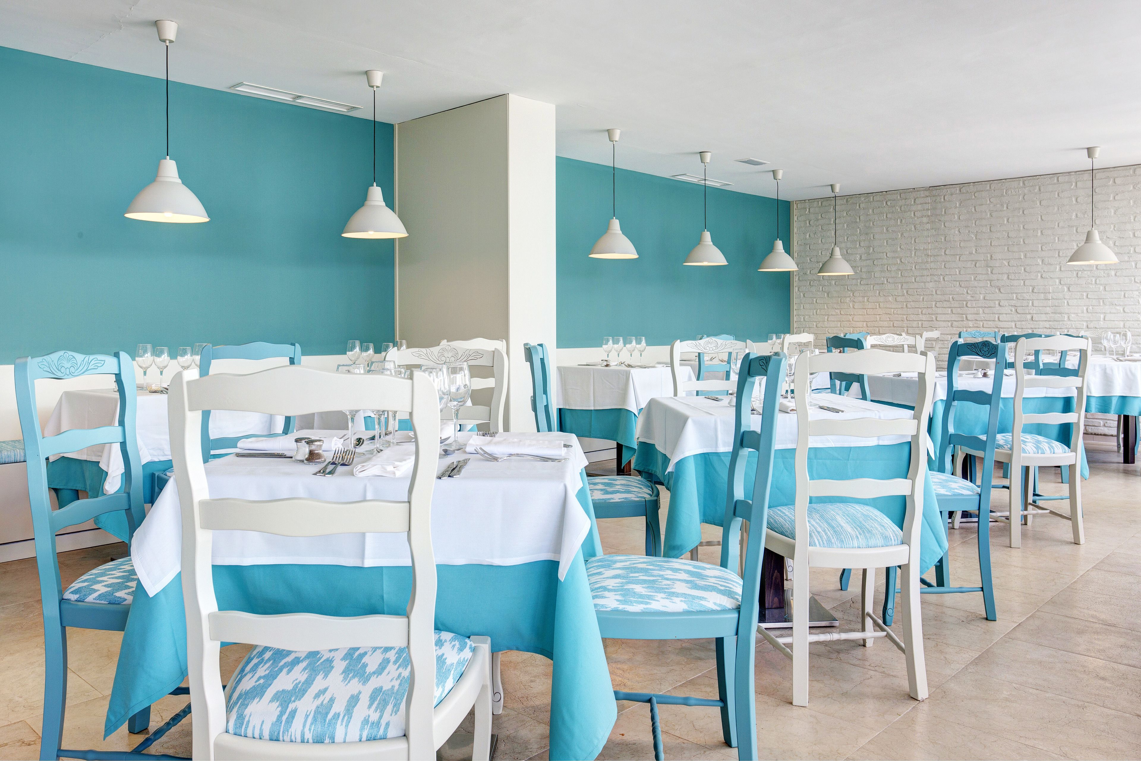 Een eetruimte met meerdere tafels en stoelen, elk voorzien van een witte tafelkleed en blauwe stoelhoezen.
